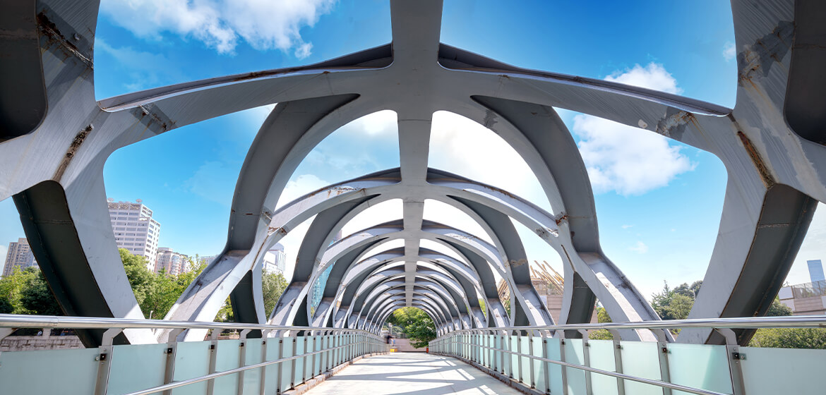Modern pedestrian bridge with artistic arch design under blue sky.